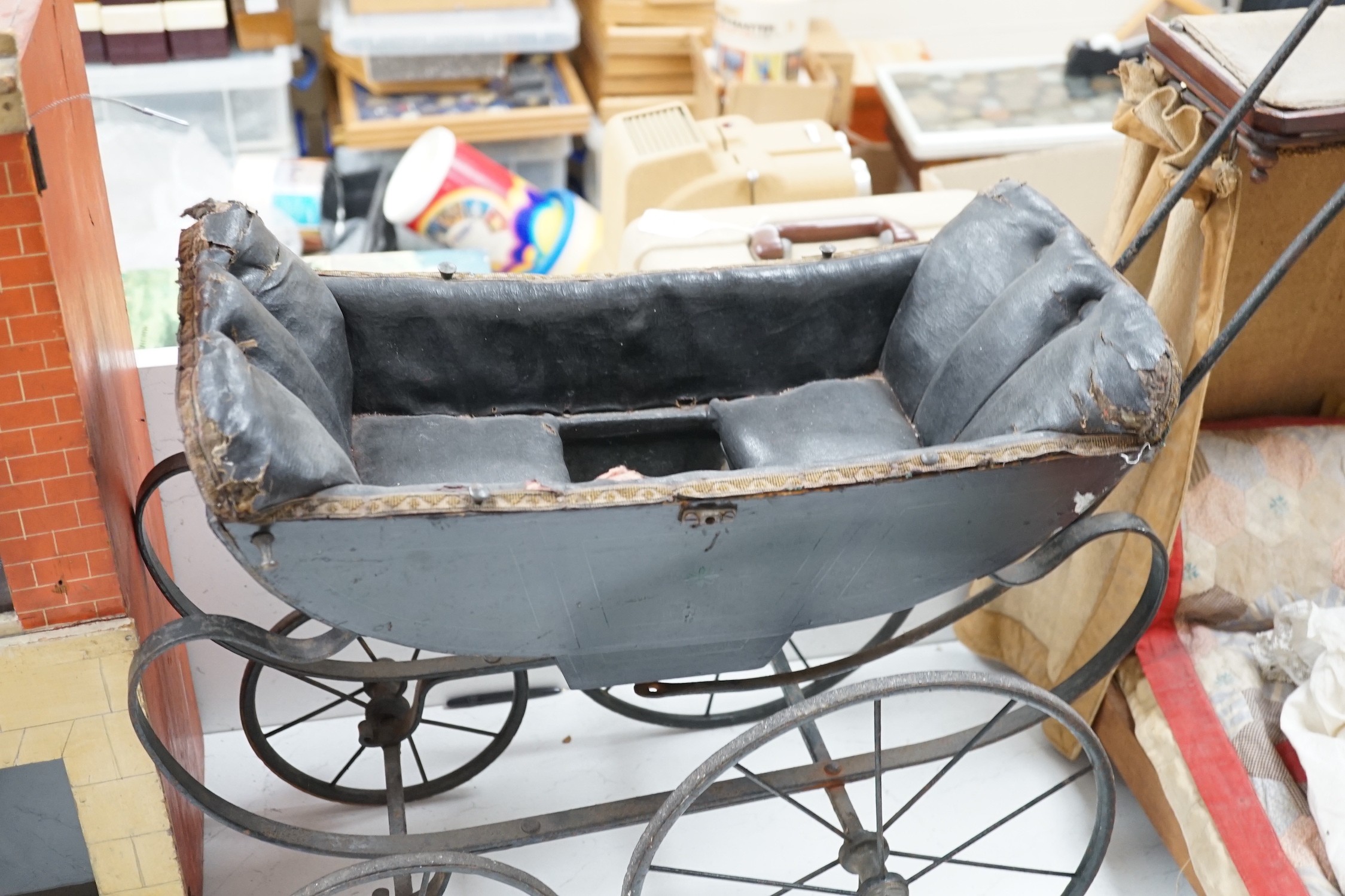 A late 19th century dolls’ pram, circa 1880, on a wrought iron chassis with spoked wheels, upholstered interior and porcelain handle, 75cm high, 90cm long